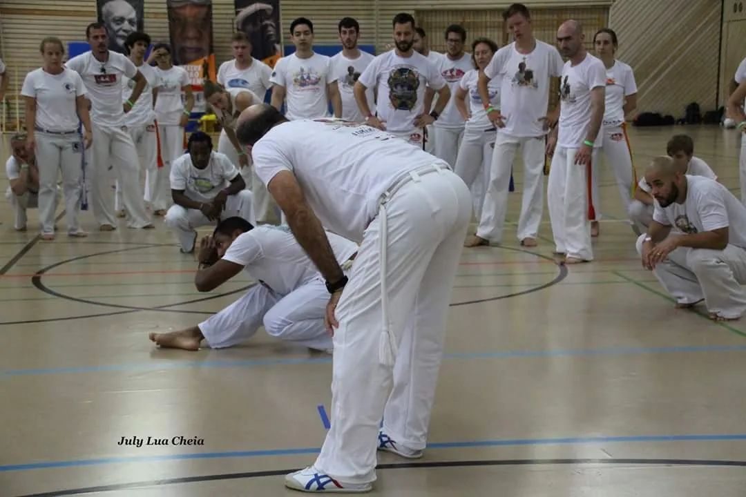 Personas adultas jugando capoeira en la roda mientras el resto del grupo canta alrededor