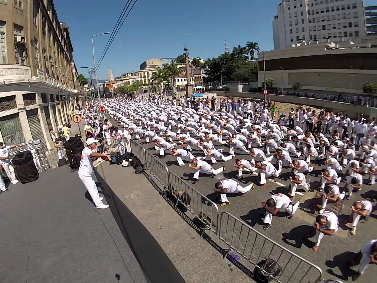 Cientos de capoeiristas de blanco arrodillados en la calle durante un gran evento de ABADÁ-Capoeira