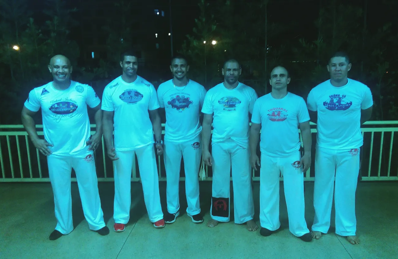 Grupo de capoeiristas con camiseta turquesa posando de noche después de una exhibición