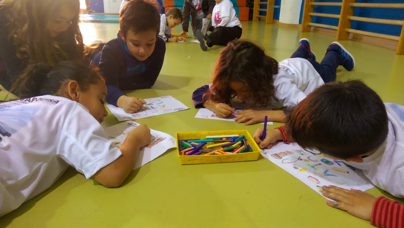 Niños y niñas tumbados en el suelo dibujando con ceras durante una actividad de la escuela