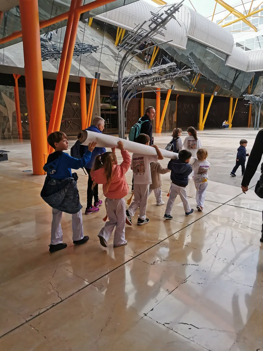 Grupo de niños con uniforme blanco caminando en fila por un recinto ferial
