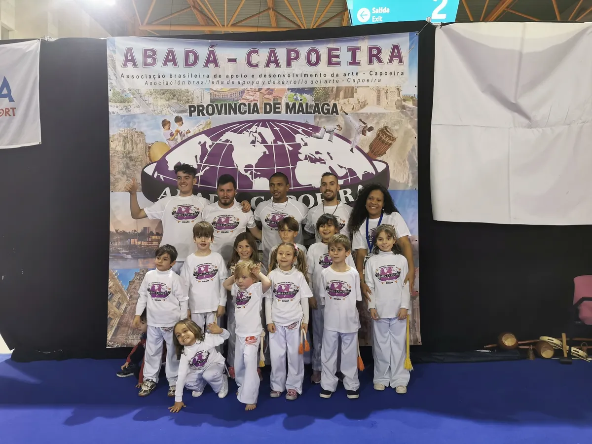 Grupo infantil de la escuela posando delante del cartel de ABADÁ-Capoeira Provincia de Málaga