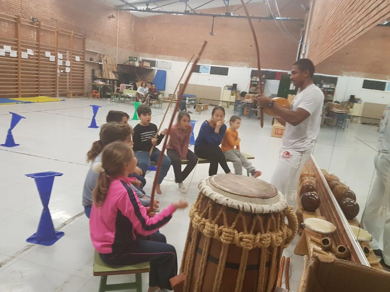 Niñas y niños sentados tocando atabaque y berimbau durante la clase de percusión