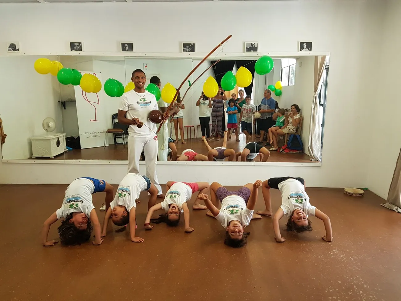 Fila de niños haciendo la ponte en el suelo de la sala mientras el Profesor Pingo toca el berimbau