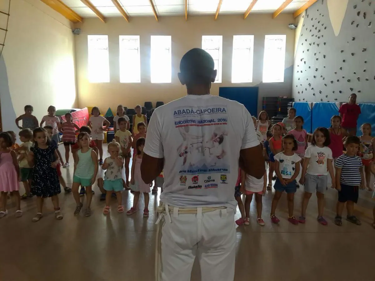 El Profesor Pingo de espaldas dando una demostración de capoeira a un grupo grande de niños en un colegio