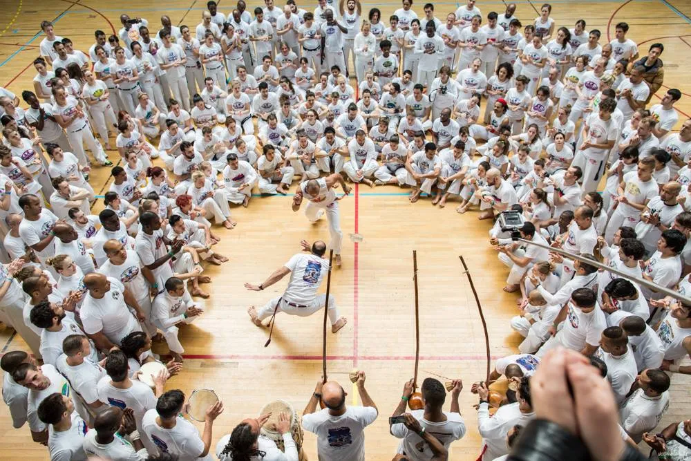 Vista aérea de una roda enorme de ABADÁ-Capoeira, con cientos de personas de blanco sentadas alrededor del círculo