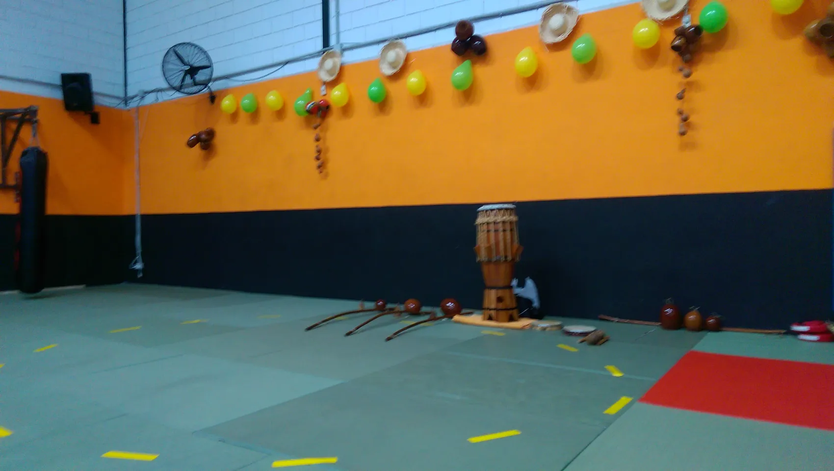 Sala de entrenamiento de la escuela, con suelo de tatami, pared azul y naranja y un atabaque apoyado en el rincón