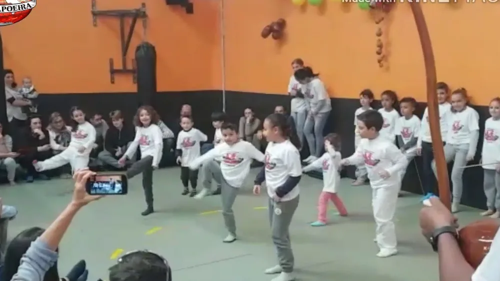 Grupo infantil de capoeira durante una exhibición con las familias mirando desde el borde de la sala