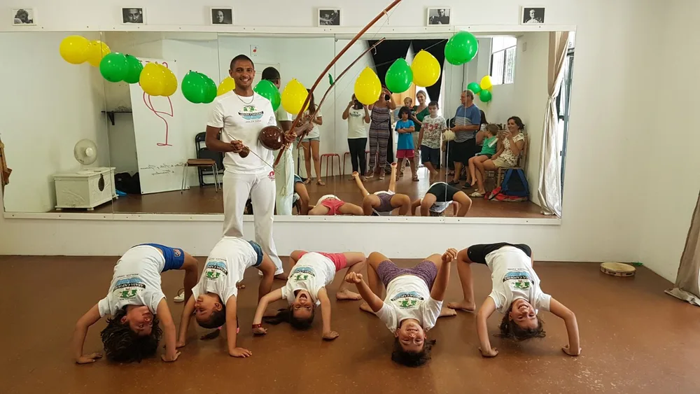 Clase de capoeira con niños haciendo la ponte mientras el Profesor Pingo toca el berimbau